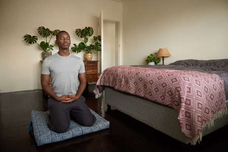 Young African man meditating on the floor of his bedroomの写真素材