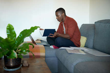 Young African man working from home on his living room sofaの写真素材