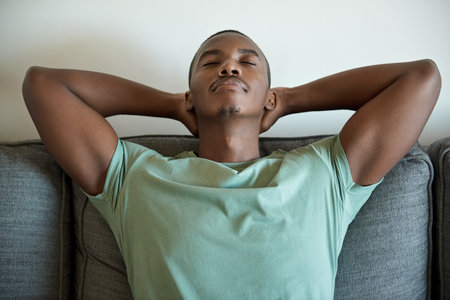 Young African man relaxing on his living room sofa at homeの写真素材