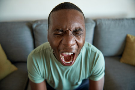 Young African man screaming in anguish at homeの写真素材