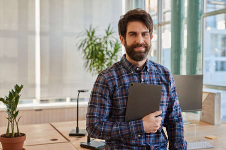 Smiling businessman leaning on his desk holding a digital tabletの写真素材