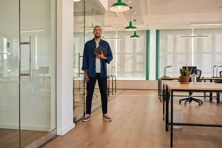 Smiling young businessman with a tablet standing in an officeの写真素材