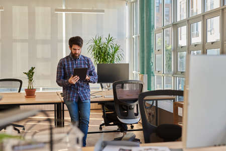Young businessman leaning on his desk working on a digital tabletの写真素材