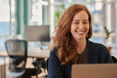 Businesswoman laughing while working on a laptop in an officeの写真素材