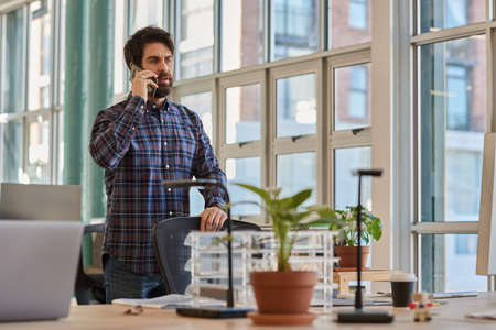 Businessman standing at his office desk and talking on a phoneの写真素材