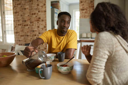 Young African man pouring coffee for his wife during breakfastの写真素材
