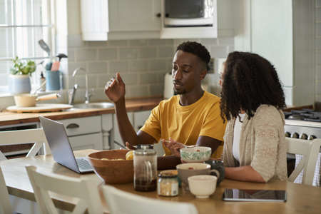 Young multiethnic couple talking and using a laptop at breakfastの写真素材