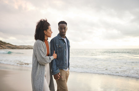 Young multiethnic couple holding hands and walking on a sandy beachの写真素材