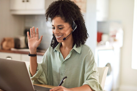 Smiling businesswoman waving during a video call while working from homeの写真素材