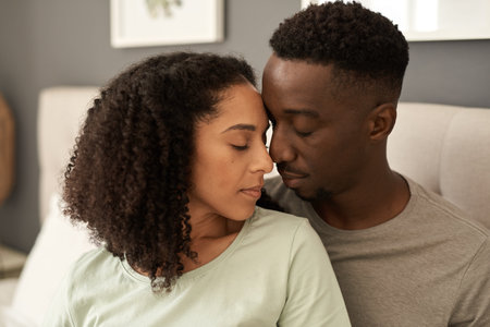 Loving young multiracial couple sitting in their bedroomの写真素材