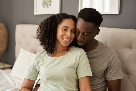 Smiling young multiracial couple sitting in their bedroom in the morningの写真素材