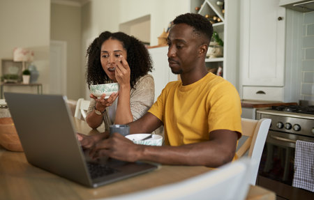 Young multiethnic couple working on a laptop during breakfast at homeの写真素材