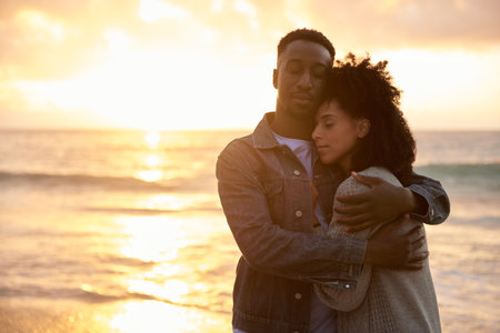 Loving young multiethnic couple holding each other on a beach at sunsetの写真素材