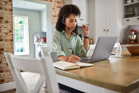 Businesswoman writing notes during a video call while working at homeの写真素材