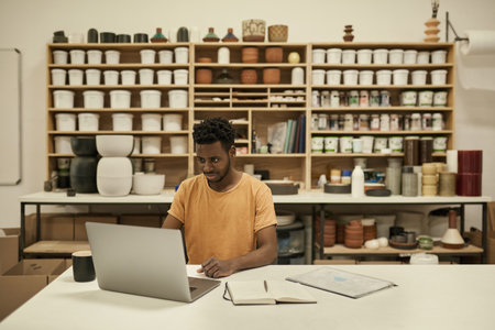 African ceramics workshop manager using a laptop in a studioの写真素材
