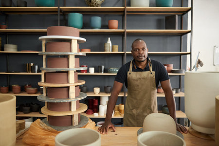 African ceramist standing at a table of pots in a studio