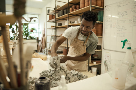 Smiling African ceramist mixing clay in a pottery studio