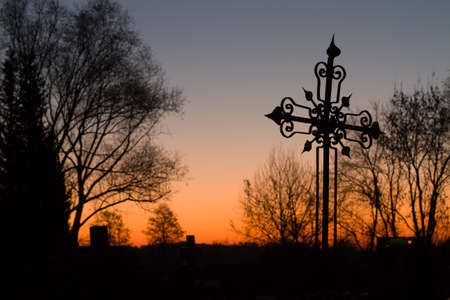 The silhouette of a metal forged cross in a cemetery before sunrise