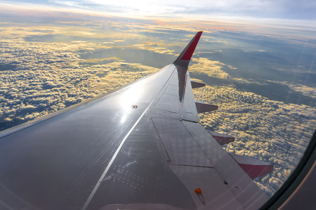 Sunset, cloudy sky and airplane wing as seen through window of an aircraft.