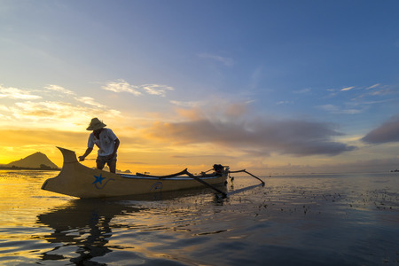 LOMBOK, INDONESIA - FEBRUARY 23, 2016: Unidentified fisherman ready to work in the boat early morning during sunrise moment. Fishing is the main occupation for the villagers.のeditorial素材