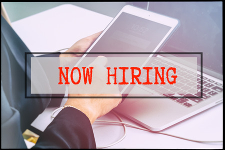 Hand and text NOW HIRING with vintage backgound. Technology concept.の写真素材