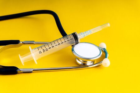 Stethoscope and syringe with yellow background.
