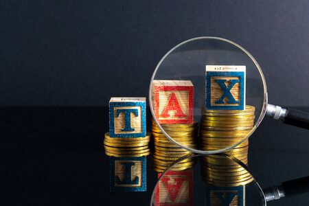 Magnifier glass and coins stacking and tax letter cube with low light view.の写真素材