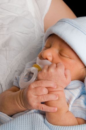 Newborn baby boy holds his pacifier in while taking a nap