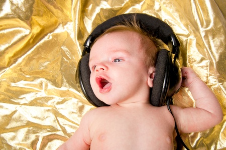 Baby boy on gold background sings along with music from headphonesの写真素材
