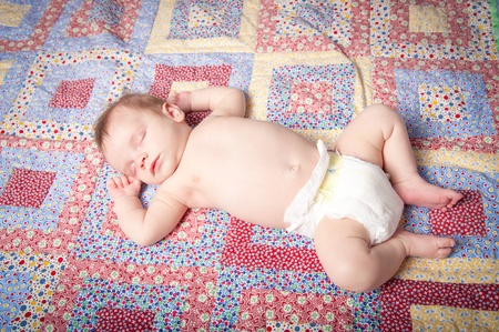 Sleeping baby boy in diaper on colorful quiltの写真素材