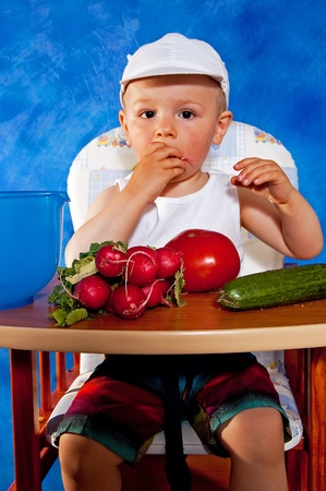 Short boy playing with vegetables against the blue mosaic backgroundの写真素材