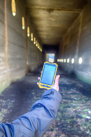Gadgets for travelers: trekking and adventure. Mountain road (pedestrian tunnel) and mobile device with blank screen (paste contents himself)の写真素材