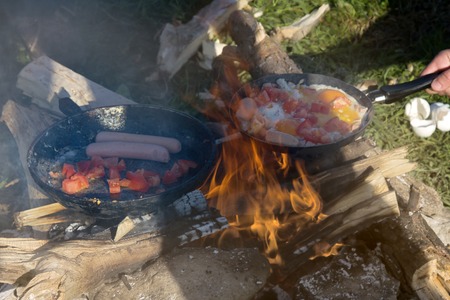 Breakfast on nature of a picnic. scrambled egg fried on coals in a pan on fireの写真素材