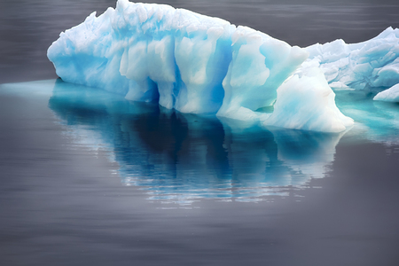 Blue growler (piece of iceberg) with reflection in calm water. Iceberg as danger to navigation and...