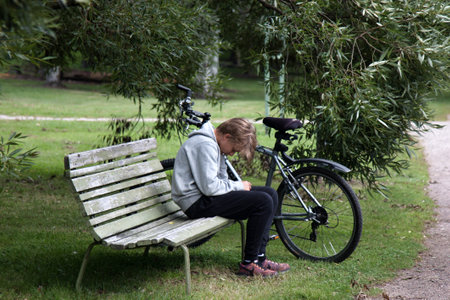 HELSINKI, FINLAND - AUGUST 21, 2017: Tired young cyclist on bench in park. Street sceneのeditorial素材