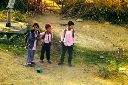 India, Jaisalmer - March 5, 2018: three Indian children near a source of drinking water. Little students. Daily life in Indian cities and villages, street photo sketchesのeditorial素材