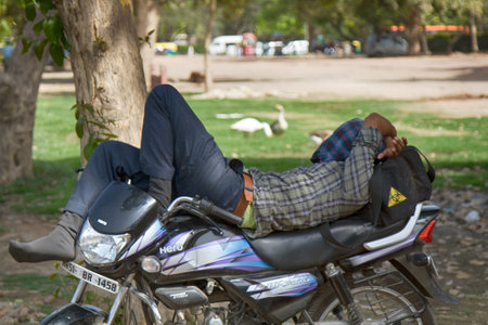 India, new Delhi - March 26, 2018: motorcyclist sleeping on a motorcycle in a city Parkのeditorial素材