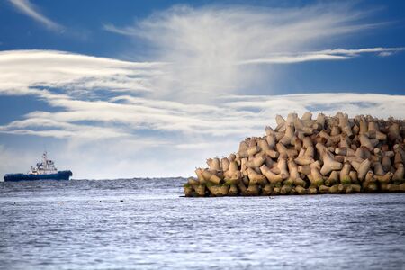 The seawall around the sea port facilities is made of concrete tetrapods (traveling-wave protection), rubble-mound breakwater. Duty marine tug. Unusual clouds over autumn sea and fedeeng marine ducksの写真素材