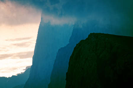 Powerful series of rocks goes into sea. Rocks at sunset in a fog of clouds in mountains and seaの写真素材