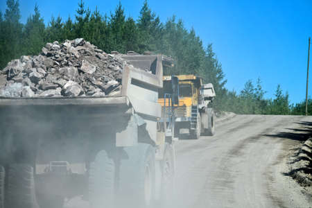 Open-pit operation. Pit dump truck, large-capacity dump truck rides on a gravel wet road works in a...