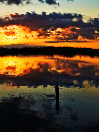 Fishing at sunset. Catching predatory fish on spinning. Sunset colors on the water surface, sunny path from the low sun. Perch caught on yellow spoonbaitの写真素材