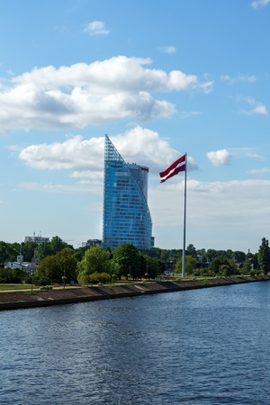 Modern glass skyscraper of Swedbank office and Latvian flag against blue sky in Riga city, Latvia, July 25, 2018のeditorial素材
