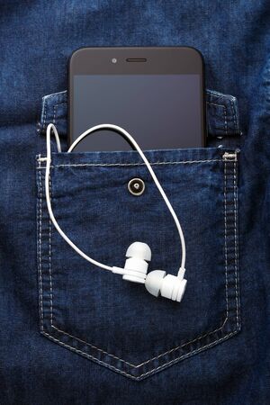 smartphone mobile in Blue jeans shirt pocket with black screen and white earphonesの写真素材