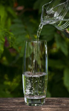 pouring Glass of clear water from jug on nature background.