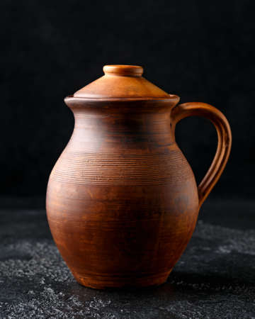 rustic handmade brown clay jug with lid on black background.の写真素材