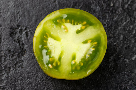 halved fresh green zebra tomato on black stone backgroundの写真素材