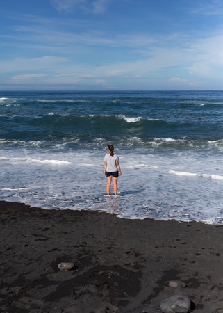 Young woman standing on a beach and looking at ocean waves in Tenerifeの写真素材