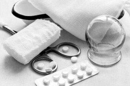 Retro. Glass medical jar, steel surgical clamp, bandage, pills, gauze cloth, metal patch on a white background of fabric. Black and white photographyの写真素材