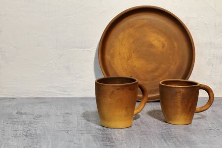 Round clay tray near the white concrete wall and clay coffee cups on a dark concrete tabletop
