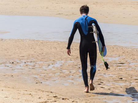 Surfer walking into the warter on the sun at the beachの写真素材